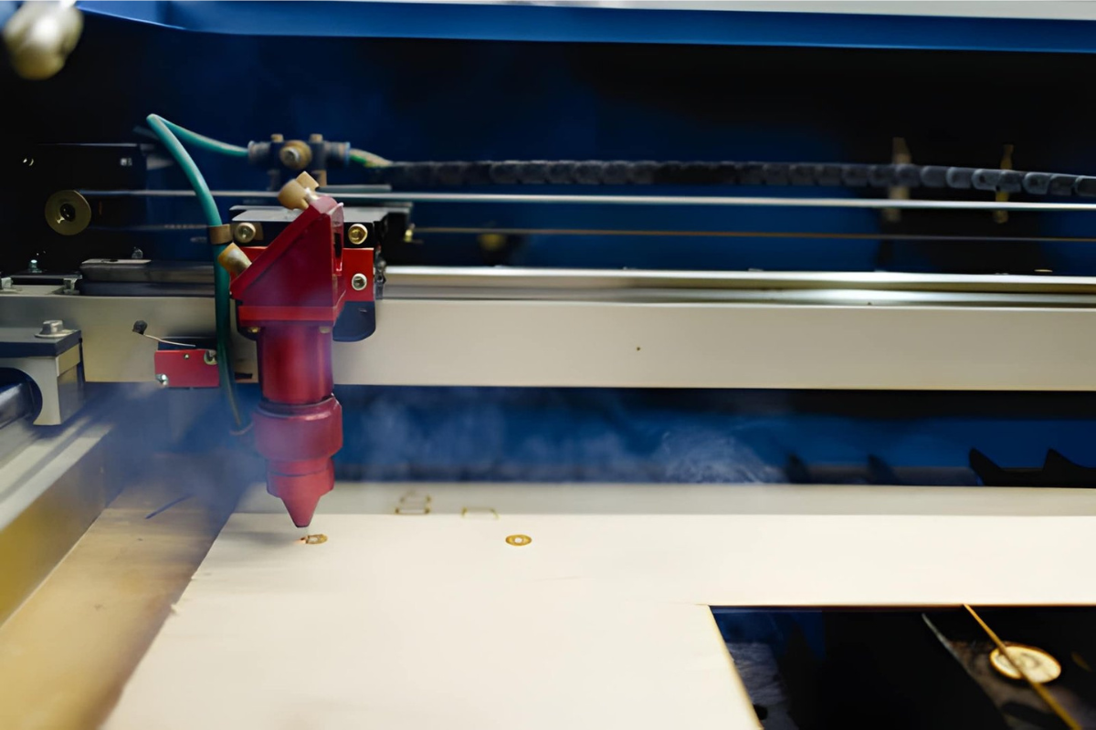 Tête laser CO₂ à buse d'assistance d'air, montée sur portique, en train de découper un panneau de bois clair avec dégagement de fumée