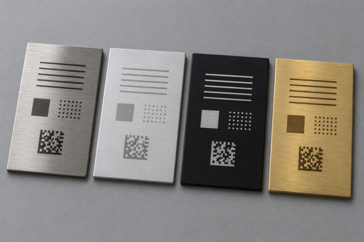 Quatre plaquettes métalliques marquées au laser fibre — acier inoxydable brossé, aluminium brut, aluminium anodisé noir et laiton — montrant quatre rendus de contraste différents pour un même motif